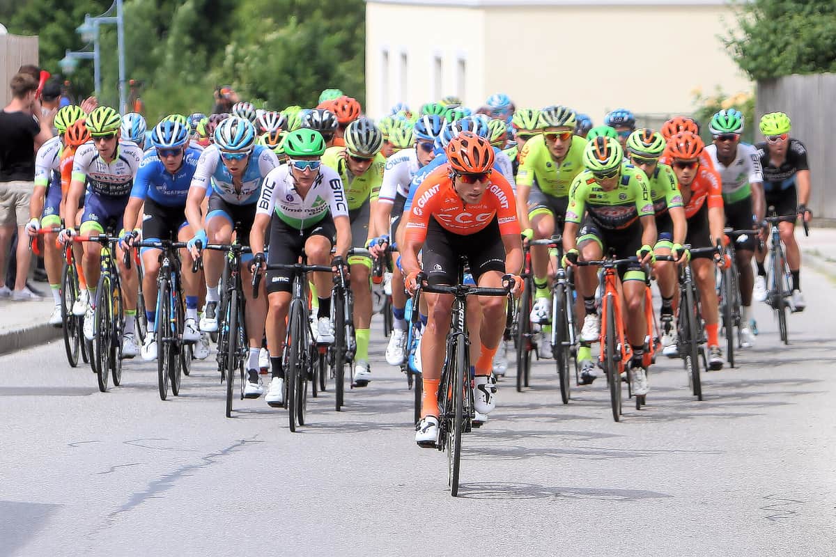 Peloton silničních cyklistů v závodě, všichni jedou v helmách